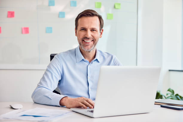 istock Professional businessman smiling while working on a laptop at his desk in office. 2169874740