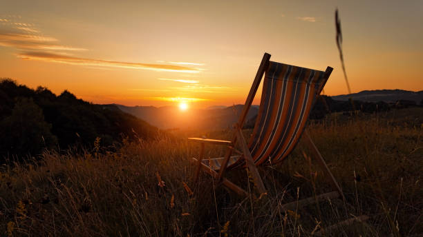 Mature man relaxes on chair in mountain meadow and watches sunrise, Canadian Rockies