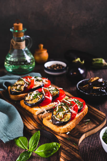 istock Fried toasts with grilled eggplant, tomatoes and cheese on a board on the table vertical view 2169899764