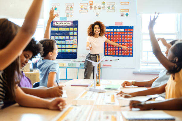 istock Smiling teacher engaging with enthusiastic diverse elementary students raising their hands in a bright, colorful classroom setting. 2169899771