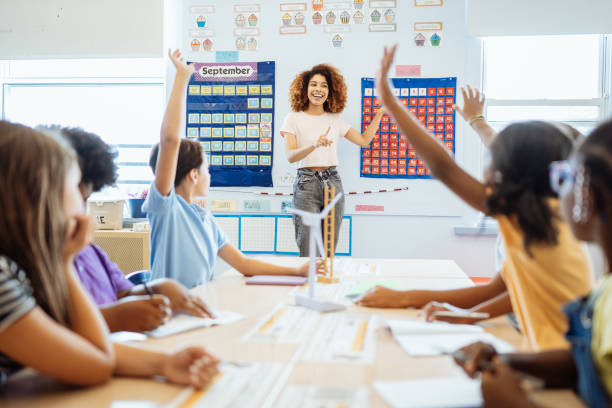 istock Smiling teacher engaging with enthusiastic diverse elementary students raising their hands in a bright, colorful classroom setting. 2169899779