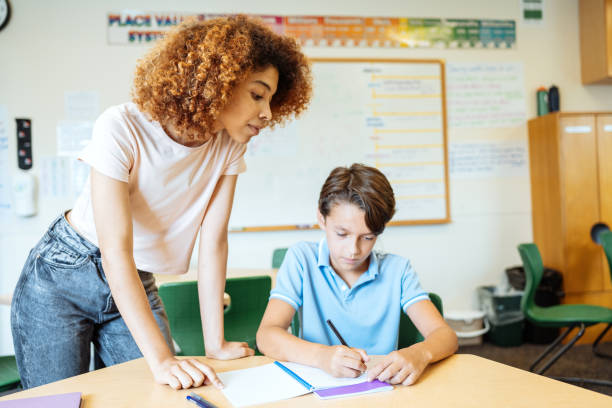 istock A millennial Latina teacher helping a young student with his writing assignment in a classroom setting, fostering education and learning. 2169899784