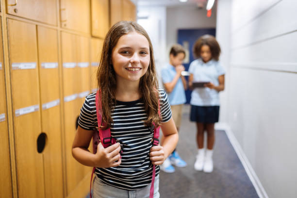 istock Schoolgirl carrying a backpack, smiles confidently in the school hallway while two classmates in the background look at a tablet. 2169899834