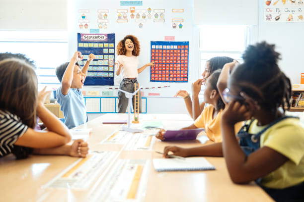 istock Smiling teacher engaging with enthusiastic diverse elementary students raising their hands in a bright, colorful classroom setting. 2169899895