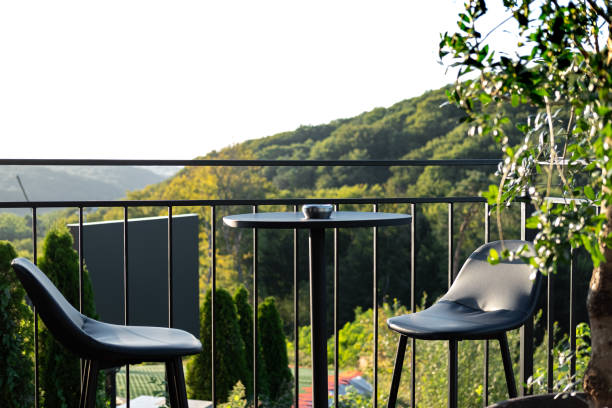 istock balcony setting featuring two modern chairs and a small table, offering a picturesque view of lush green hills under a clear sky. 2169902856