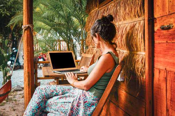 istock Back view caucasian hipster woman sit by computer outside eco-friendly straw house building guesthouse. Freelance work in south-east asia remotely isolated in tropical nature concept 2169904849