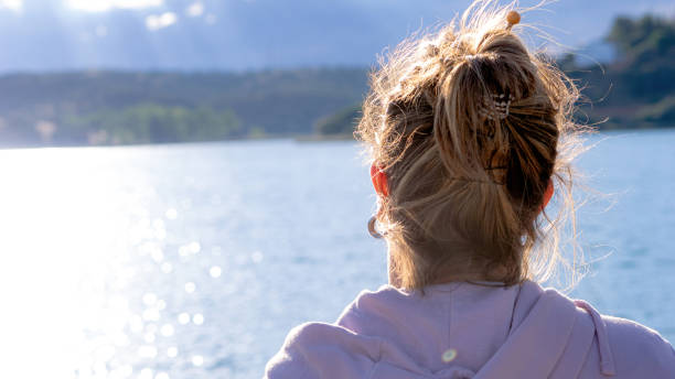 A woman with her back turned in the foreground looking at a lake