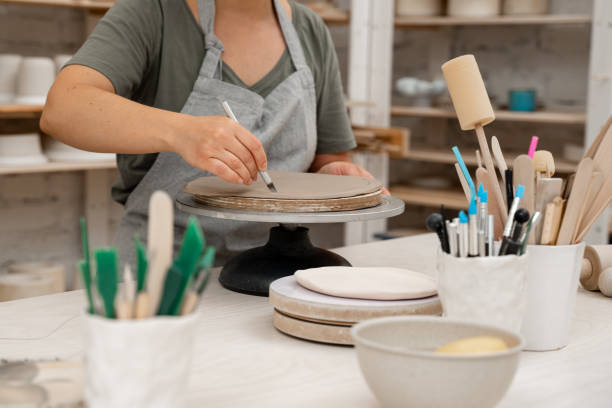 istock Girl is modeling clay into a round form. Using a sharp pottery carving knife to cut out a perfect round shape from clay. Ceramics class. 2169933507