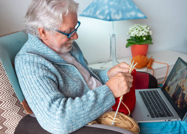 istock Senior man at home follows online knit tutorial to relax enjoying resting home leisure activity sitting on armchair - male people knitting with computer class help - people inner lifestyle hobby 2169936491