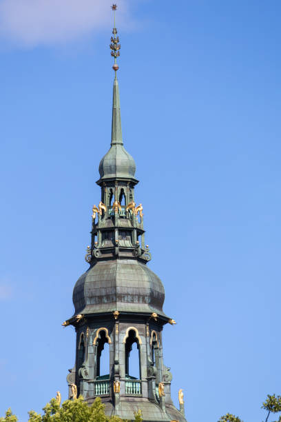 A close-up view of a historic church tower with a green copper dome and ornate details against a clear blue sky.