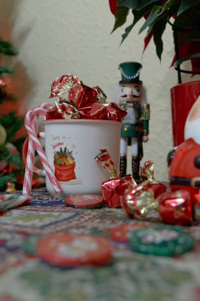 A festive Christmas mug filled with candy canes and chocolates, surrounded by more sweets and a nutcracker figure, evoking holiday cheer.