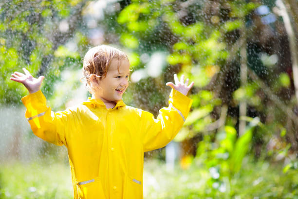 Child playing in the rain on sunny autumn day. Kid under heavy shower with yellow duck umbrella. Little boy with duckling waterproof shoes. Rubber wellies boots. Fall outdoor activity by rainy weather