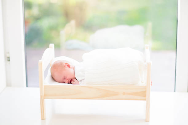 Adorable baby in white sunny bedroom. Newborn child relaxing on toy bed. Nursery for young children. Textile and bedding for kids. Family morning at home. New born kid during tummy time with toy bear.