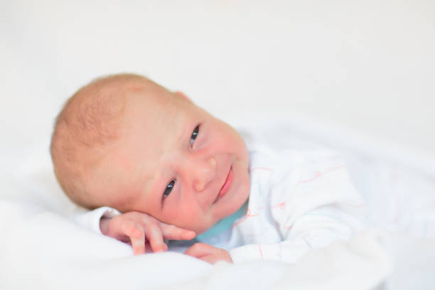 Adorable baby in white sunny bedroom. Newborn child relaxing in bed. Nursery for young children. Textile and bedding for kids. Family morning at home. New born kid during tummy time with toy bear.