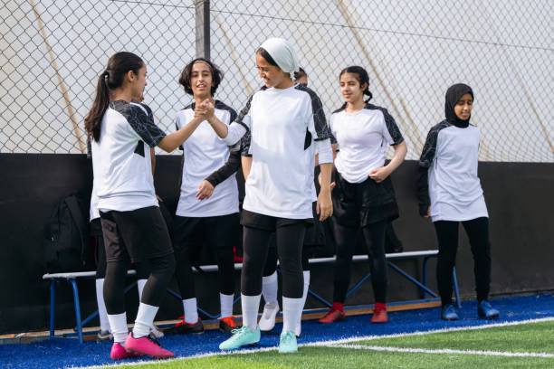 Female footballers shaking hands by soccer team Female athletes shaking hands by soccer team at training ground. Soccer players are wearing uniform. They are at sports venue. Sports Events stock pictures, royalty-free photos & images