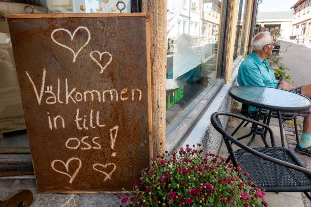 Osthammar, Sweden Aug 19, 2024 A man sits at an outdoor cafe and a sign in Swedish on the main street says Welcome to us!