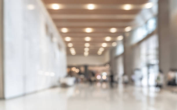 Blurred office building lobby or hotel blur background interior view toward reception hall, modern luxury lounge, white room space with blurry corridor and building glass wall
