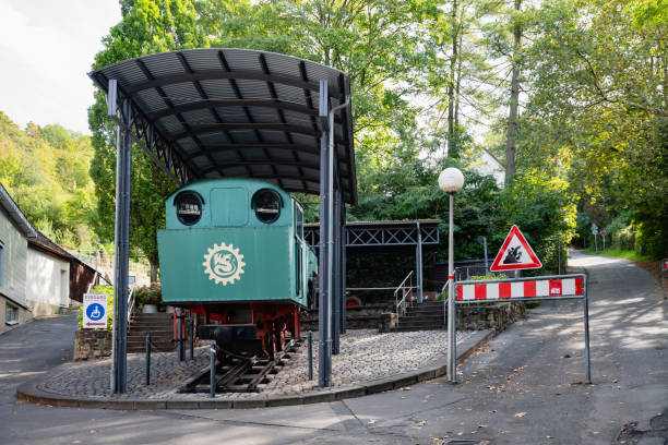 Historic Drachenfels train locomotive on display, sheltered under a canopy in a peaceful forest area. The green locomotive showcases classic railway engineering.