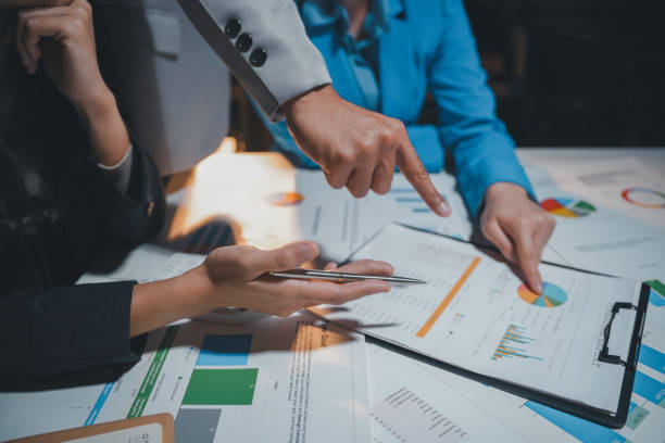 istock Business team is working late, analyzing financial documents and pointing at charts and graphs 2169965599