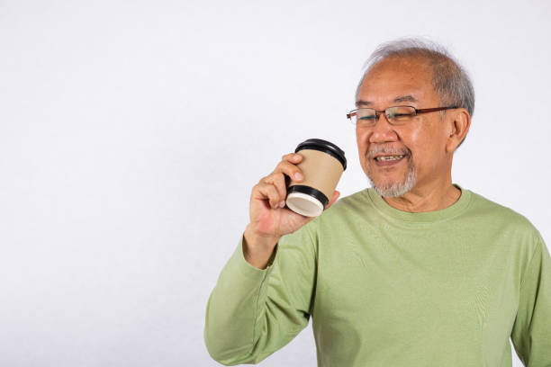 Portrait Asian old man while holding a coffee cup and smiling studio shot isolated on white background. Concept of happiness and contentment, lifestyle senior man is enjoying his coffee takeaway
