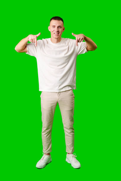 istock Young Man in a White Shirt Pointing Downward Against a Bright Green Background 2169972994
