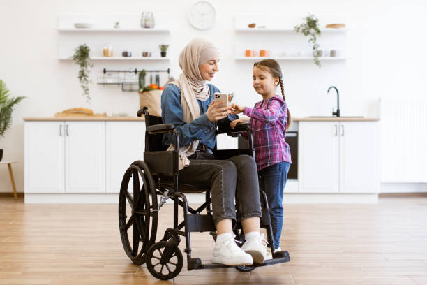 istock Muslim mother in wheelchair with daughter using mobile phone in kitchen 2169973408