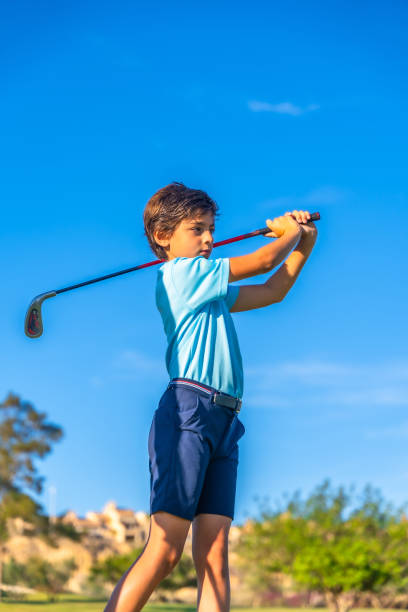 Vertical photo of a caucasian young concentrated boy swinging golf during golf lesson outdoors