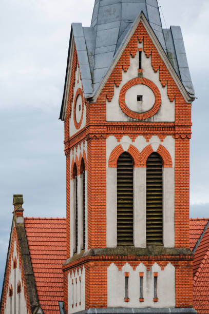 A close-up view of the intricate brickwork on the tower of a Gothic Revival church. The design features red brick patterns and arched vents, showcasing the craftsmanship and architectural detail typical of the Gothic Revival style.