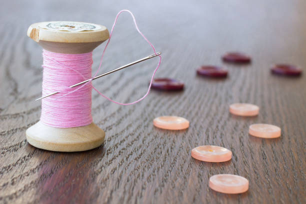 Spool pink thread with a needle. Pink and claret buttons on the table
