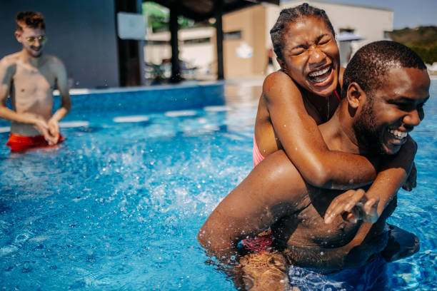 istock Friends having fun at swimming pool walking in water while carrying each other on back 2169983381