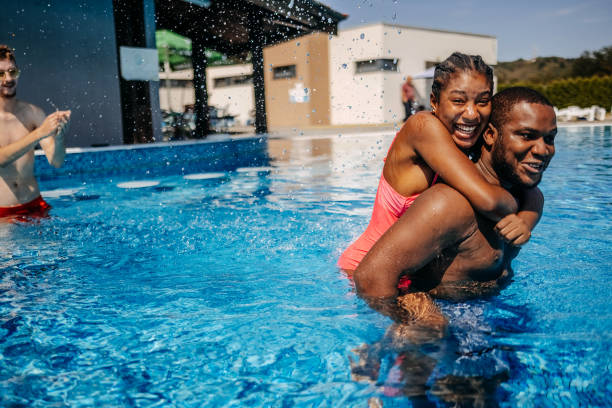 istock Friends having fun at swimming pool walking in water while carrying each other on back 2169983386