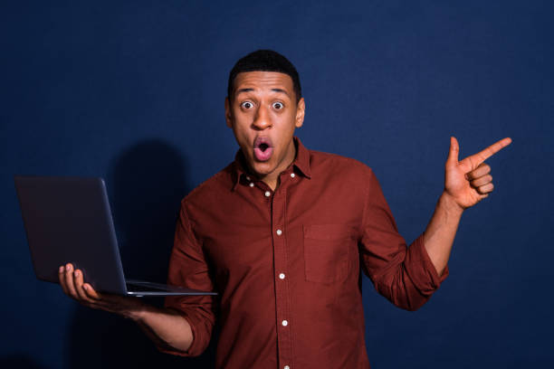 istock Photo of impressed positive guy dressed brown shirt working modern device pointing emtpy space isolated blue color background 2169987232