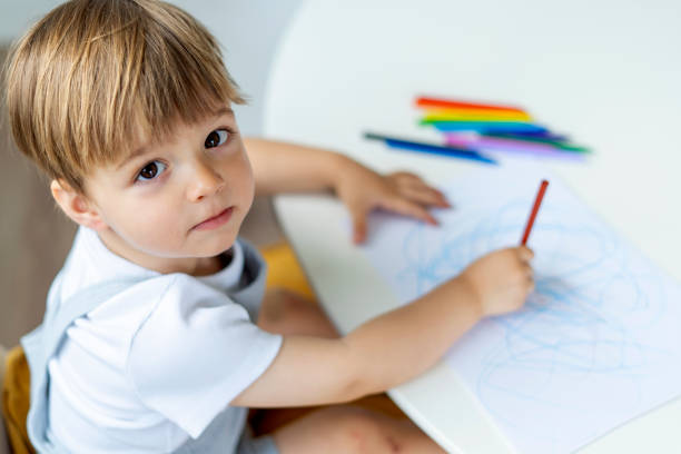istock Focused Little Boy Drawing on Paper, Surrounded by Colorful Crayons 2170002770