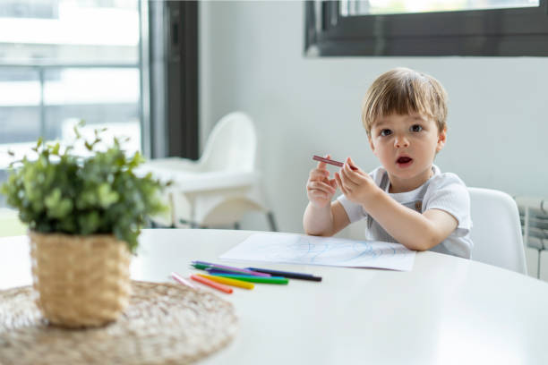 istock Little Boy Drawing with Crayons at a Table, Focused and Curious Expression 2170002775