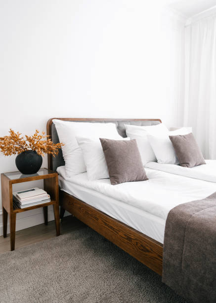 Bed, nightstand and bedside table with home decor and books against white wall