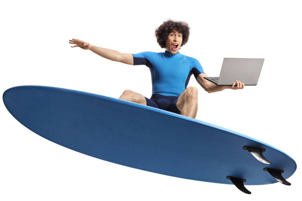 Man in a wetsuit surfing on a surfboard and holding a laptop computer isolated on white background