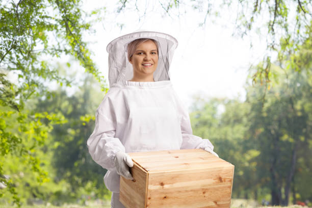 Young female bee keeper in a uniform holding a wooden box
