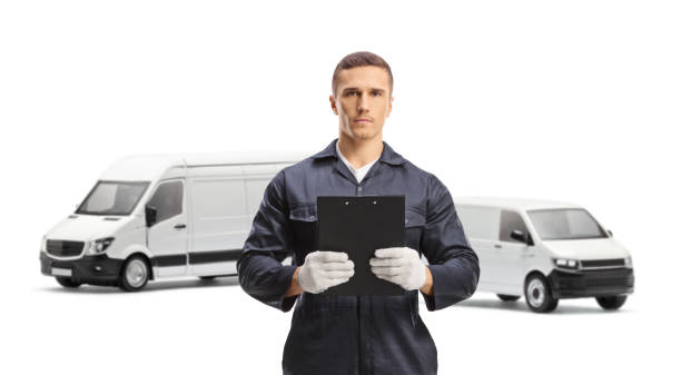 istock Mechanic in a uniform standing in front of vans and holding a document with a clipboard 2170013882