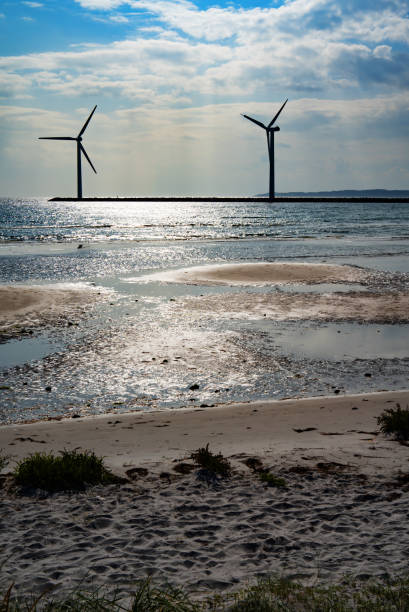Wind turbine by the sea with glittering sunshine sun and blue sky. Sustainable energy concept. Vertical background for nature conservation.