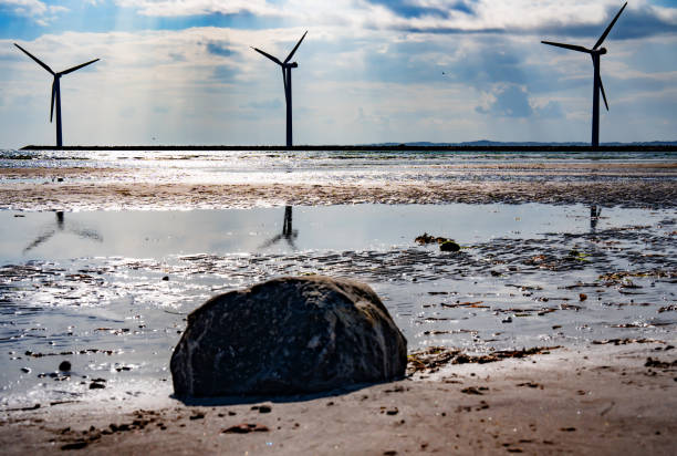 Wind turbine by the sea with glittering sunshine sun and blue sky. Sustainable energy concept. Horizontal background for nature conservation.