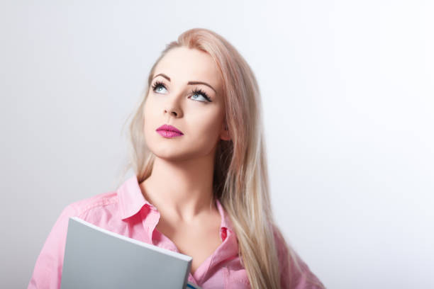 Young woman is deep in thought while holding a book, perhaps she is looking for inspiration or trying to remember something