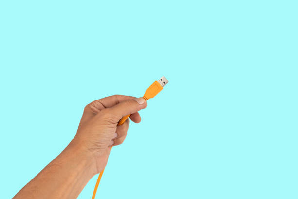 istock Male hand holding an orange usb cable isolated on cyan background 2170031943