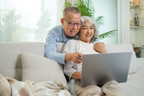 istock Elderly couple is sitting together on a comfortable sofa at home, both engaged with a laptop on the womans lap. 2170033504