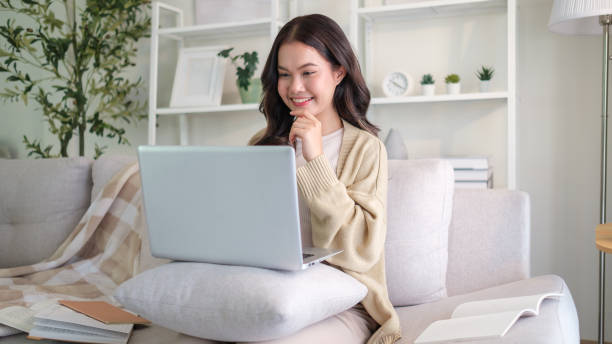 istock Young woman browsing internet on laptop while sitting on sofa in cozy living room. 2170034041