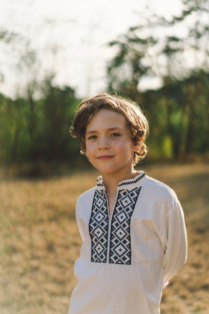 istock A boy smiles confidently while standing in a sunlit field, wearing a traditional embroidered shirt 2170035322