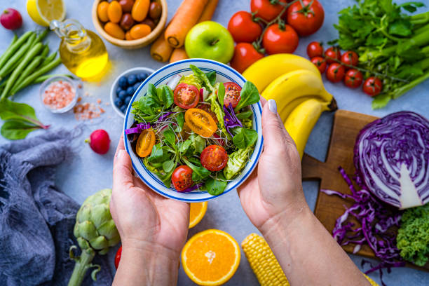 istock Hands holding fresh rainbow colored salad bowl. Multicolored fruits and vegetables background. Healthy eating and dieting concept 2170051903