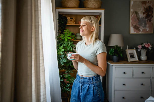 istock Woman with coffee looking through the window 2170057696