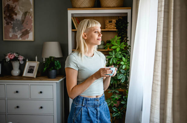 istock Woman with coffee looking through the window 2170059042