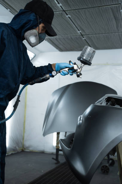 istock Car painter is changing the color of vehicle using sponge and paint sprayer. Worker is painting car in dark color with HVLP spray gun. 2170063451