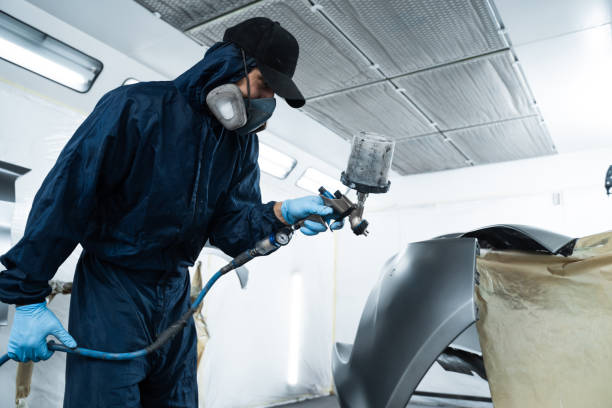 istock Mechanic from vehicle maintenance service is spreading paint on car using dark spray and paint gun. Professional worker wearing protective gloves is painting automobile. 2170063472